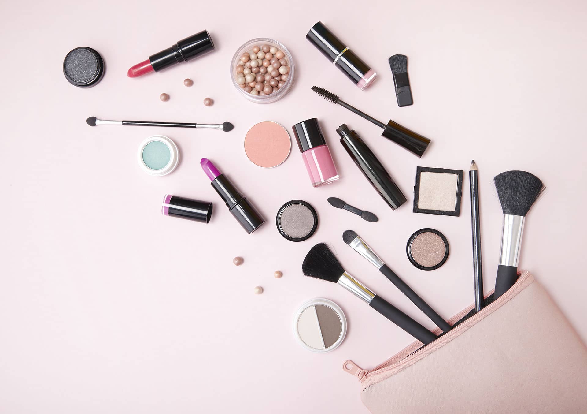 A variety of makeup products with endocrine disrupting chemicals and brushes spilling out of a bag
