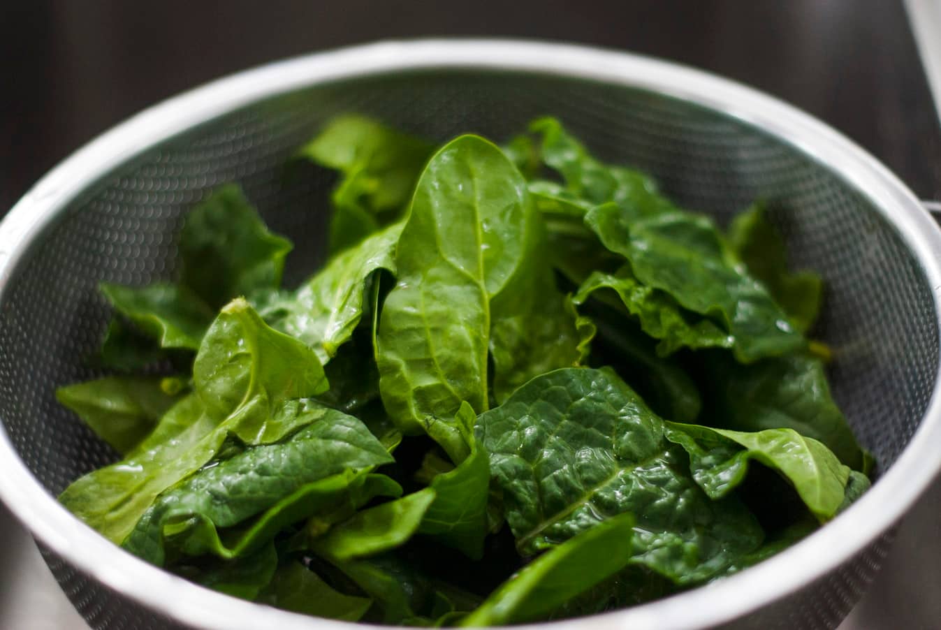 A strainer filled with fresh spinach leaves