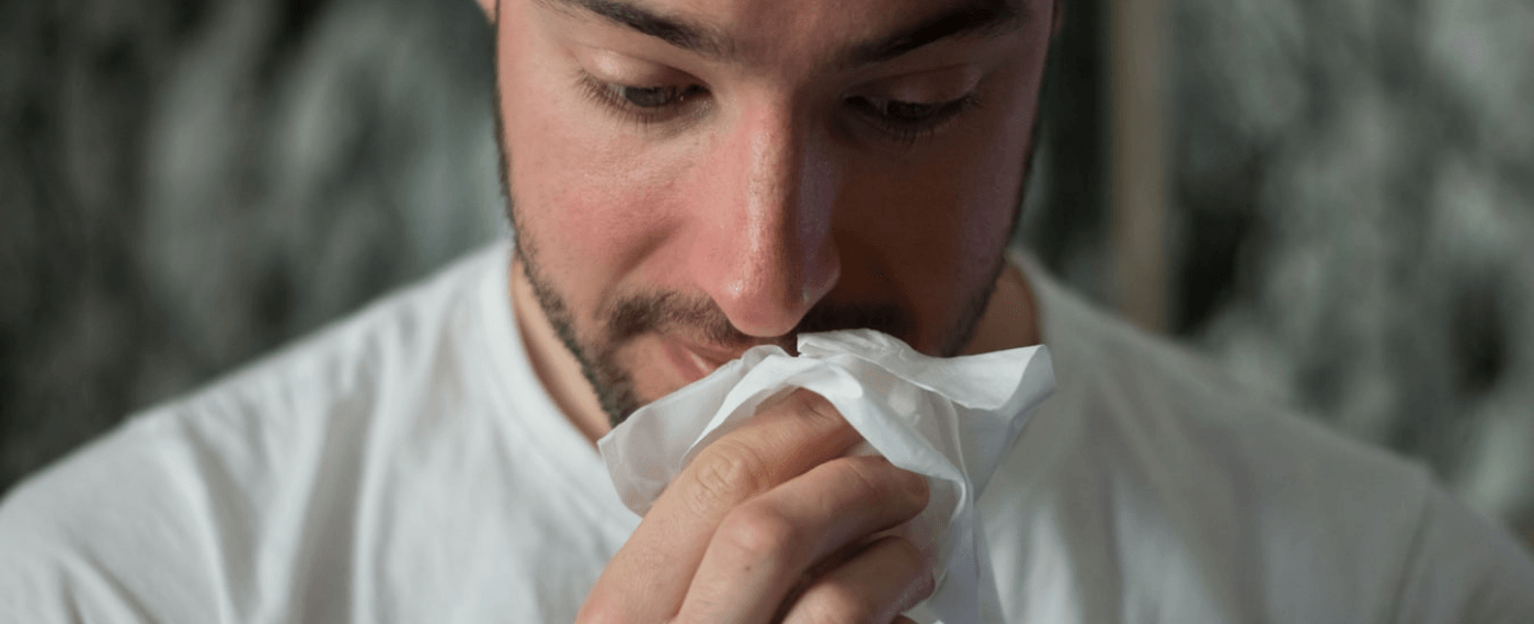 Man holding a tissue up to his nose while looking down