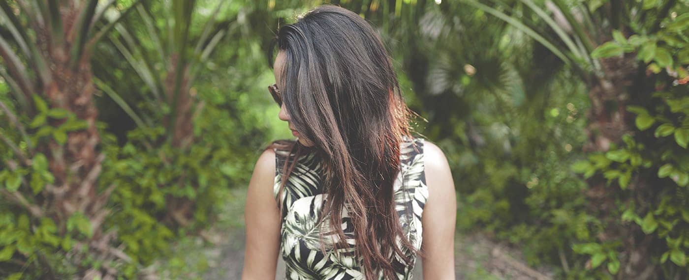 Woman wearing forest print dress with head turned in front of palm trees