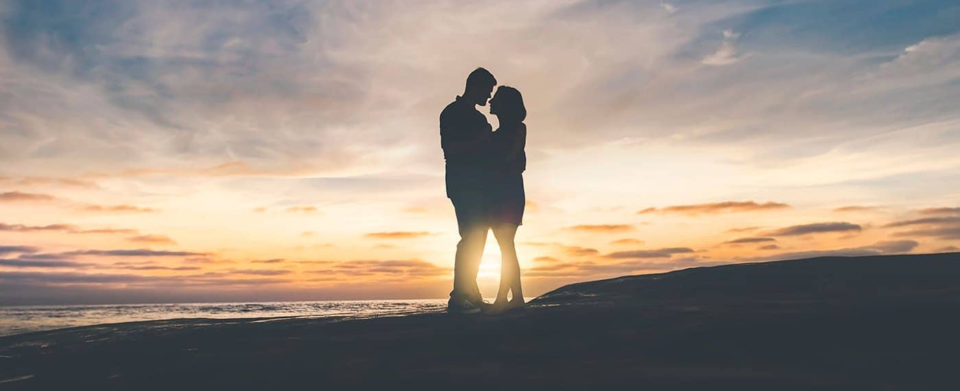 Woman and and man kissing in front of setting sun
