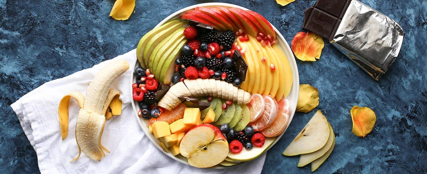 A bowl of antioxidant rich foods including bananas, berries, apples, and mango