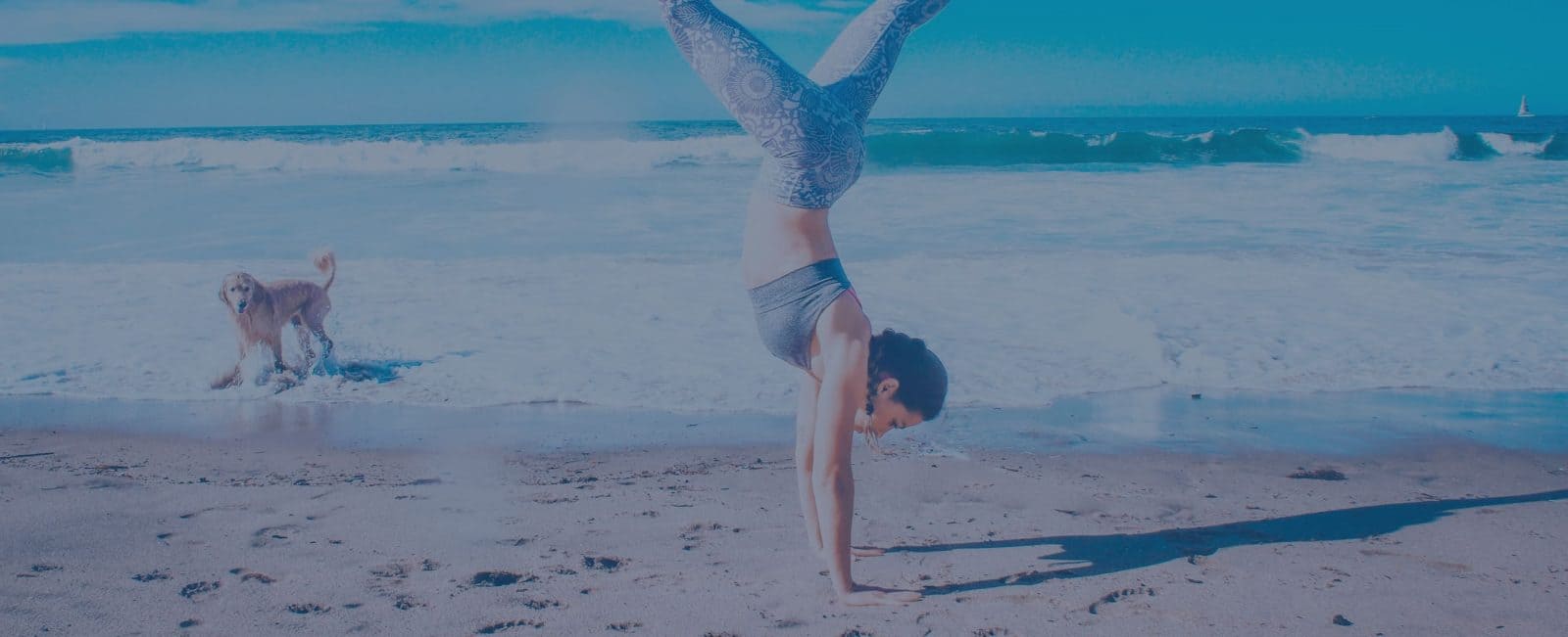 Woman doing a handstand on the beach with dog in the background