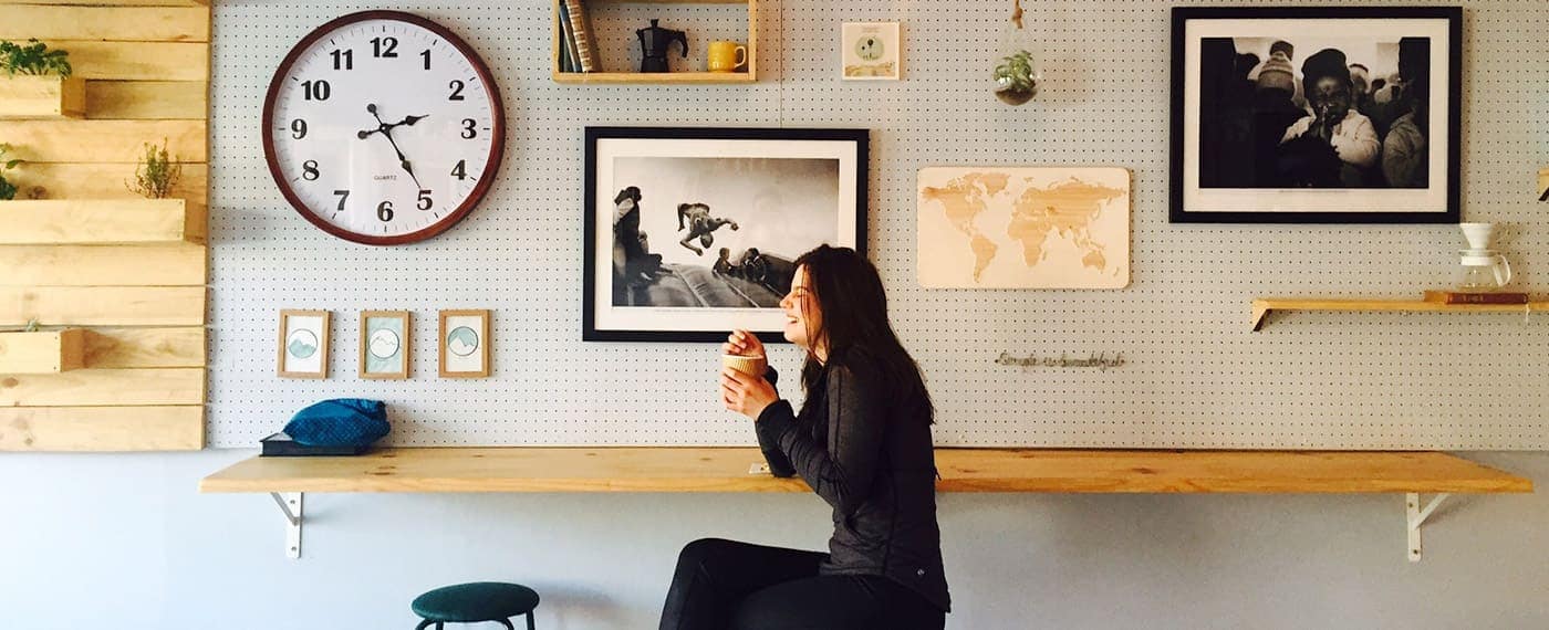 Woman laughing and drinking coffee with framed photos hanging on the walls