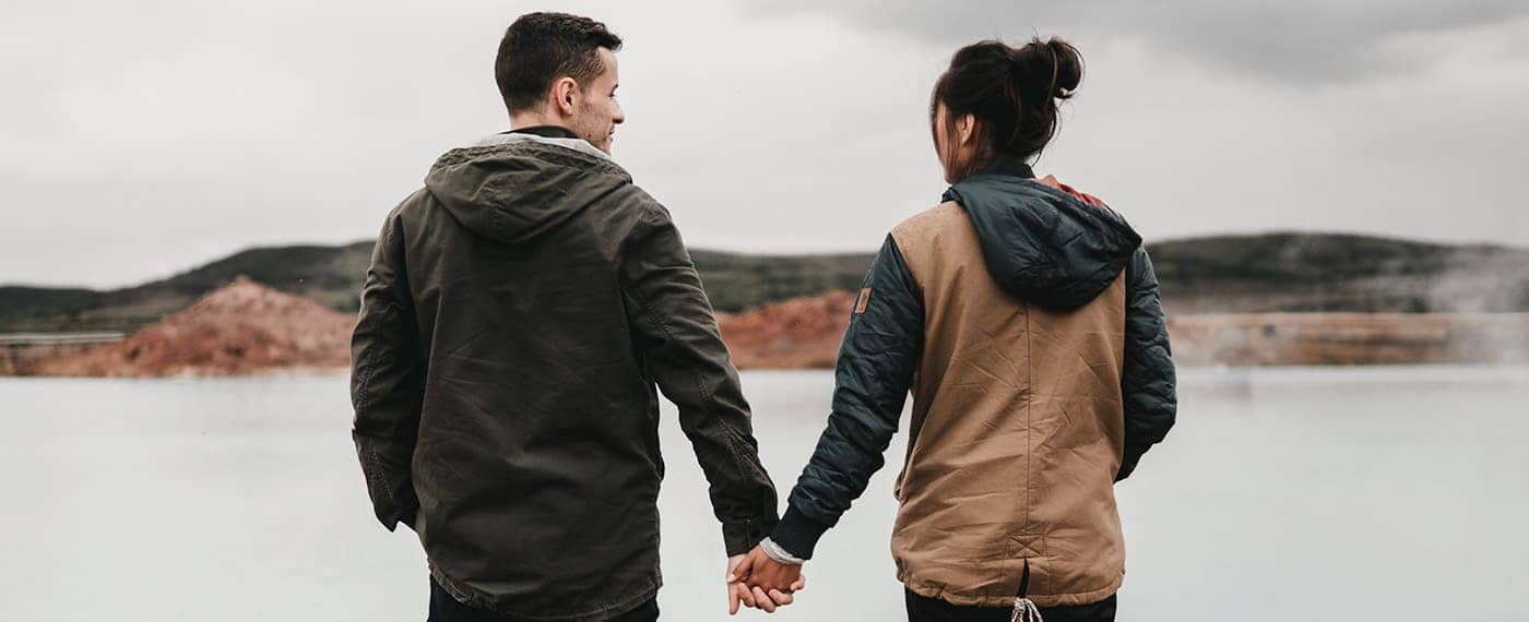 Woman and man in a relationship standing in front of lake holding hands