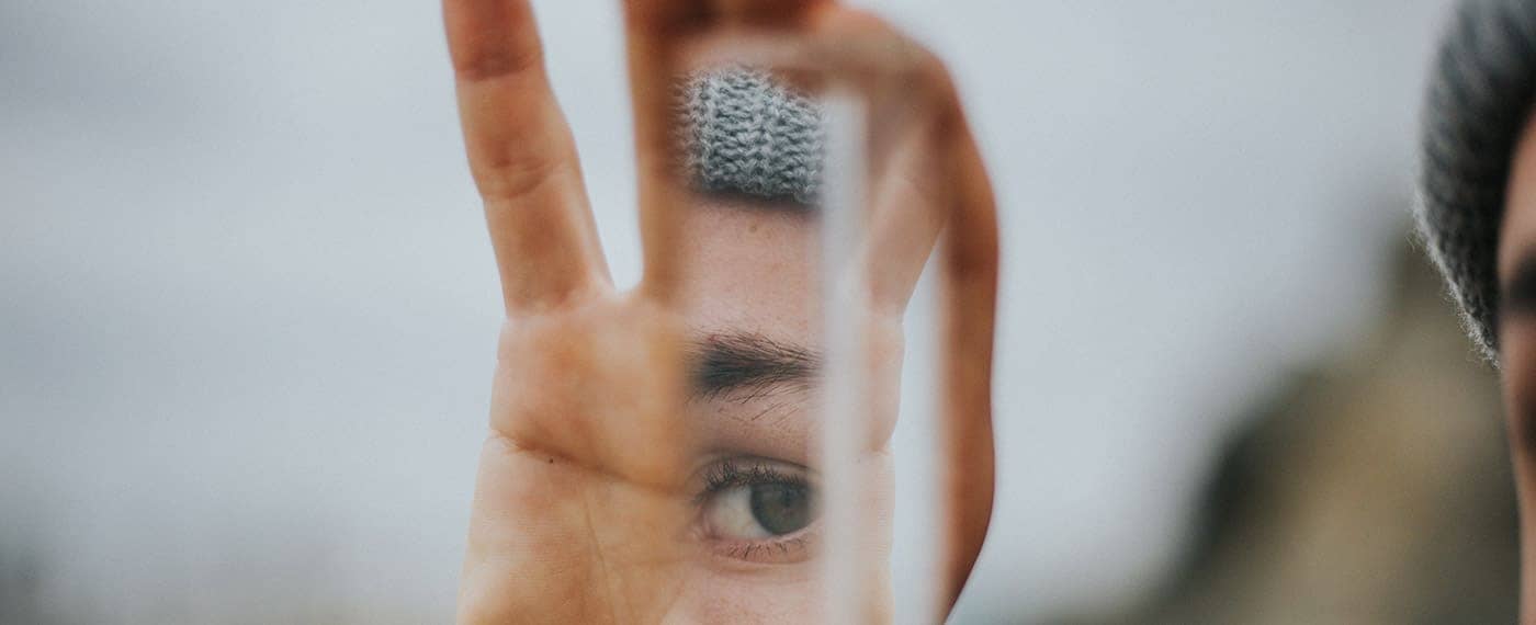Man holding up a piece of broken mirror that reflects his eye