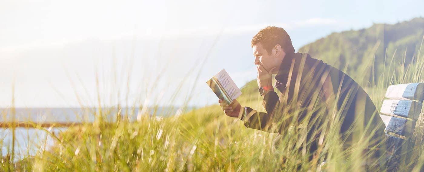 Fit man reading a book while sitting on a bench in a field
