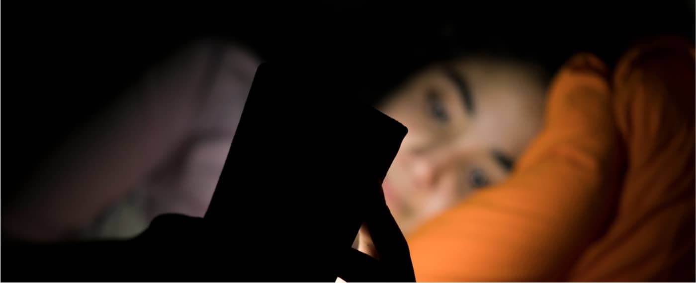 Girl looking at smartphone at night while lying in bed