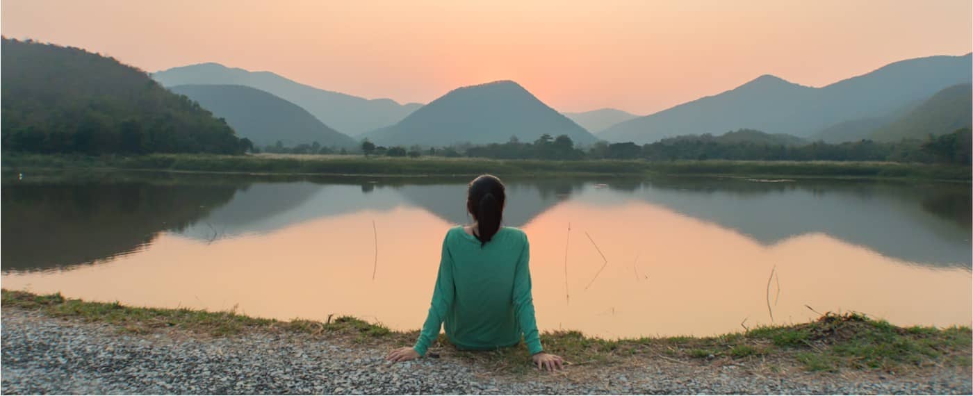 Woman sitting and being mindful of the peaceful lake water and scenery
