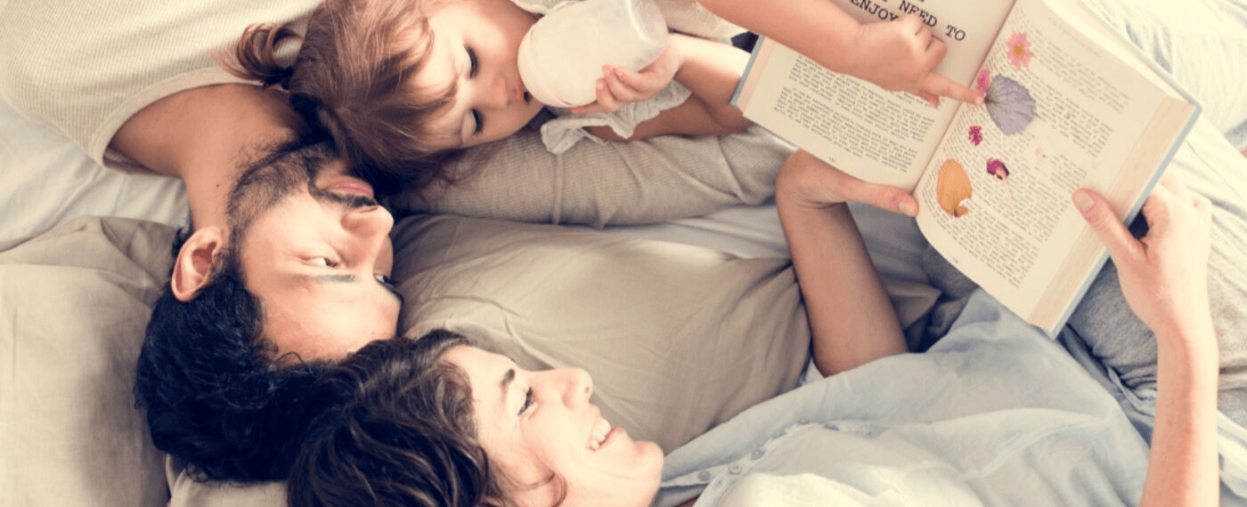 Mother and father lying in bed reading a book to daughter