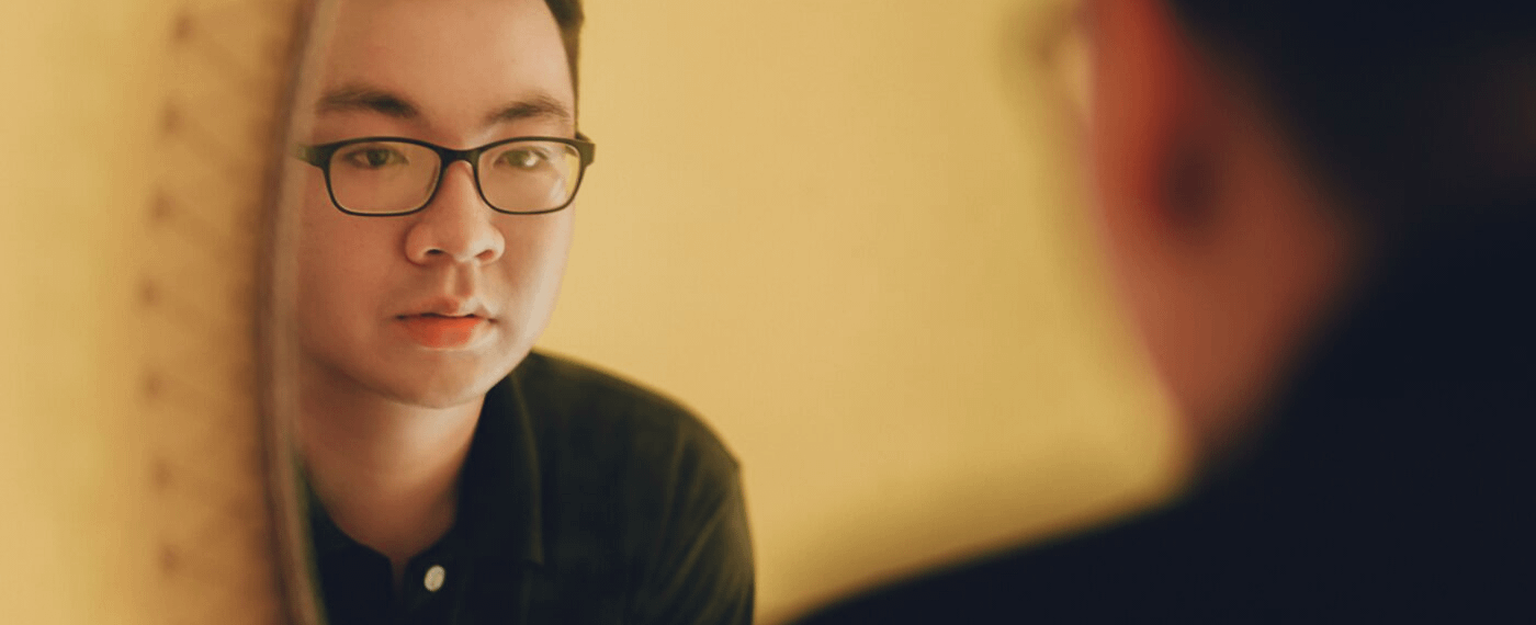 Man with glasses stares at his own reflection in the mirror