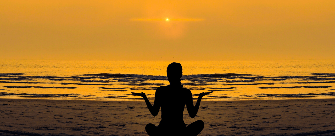 Woman meditating by the beach during sunset