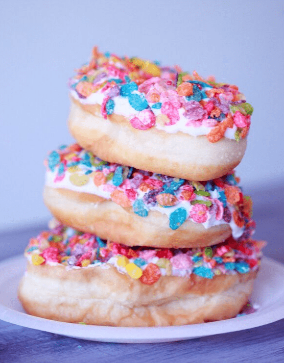 3 vanilla frosted donuts stacked on top of each other with fruity pebble sprinkles