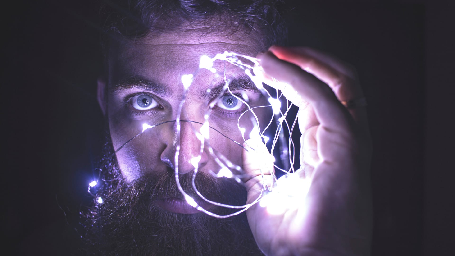 Bearded man holding up a string of led lights near his eyes