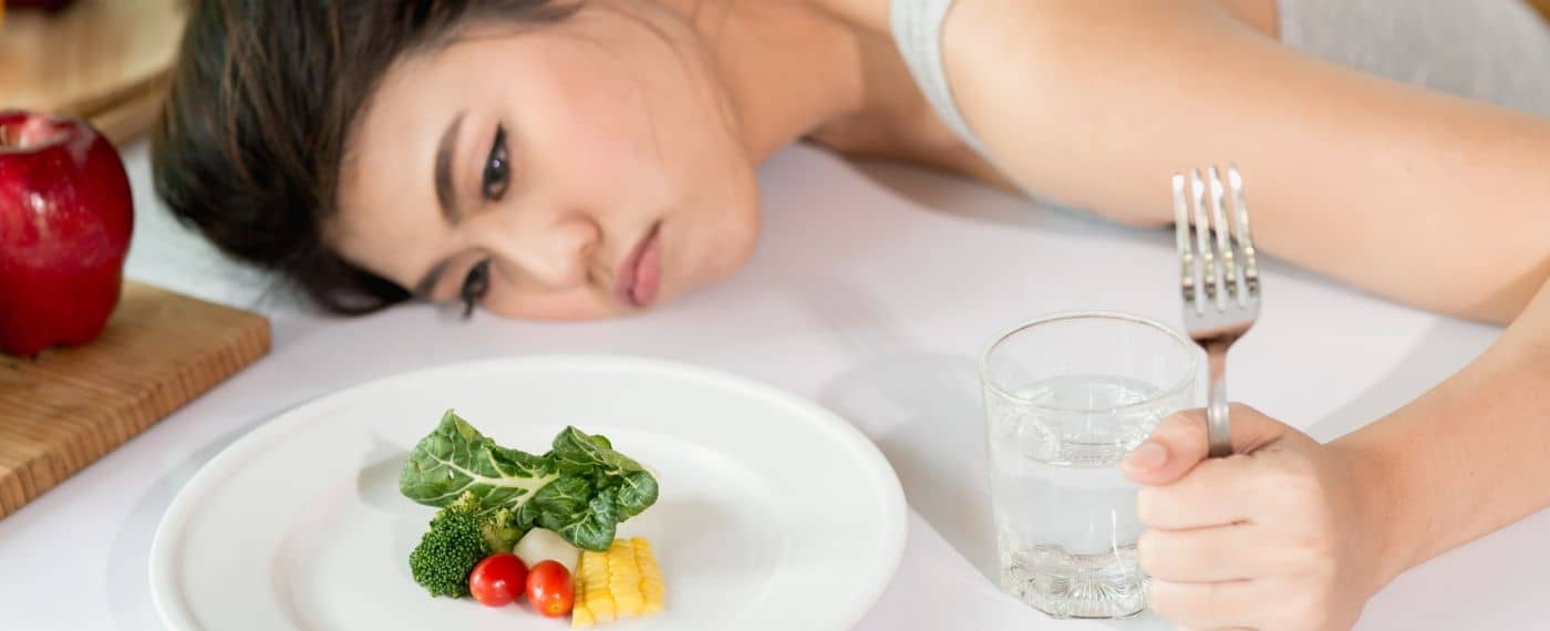 A frustrated woman stares at a spare plate of veggies in hunger