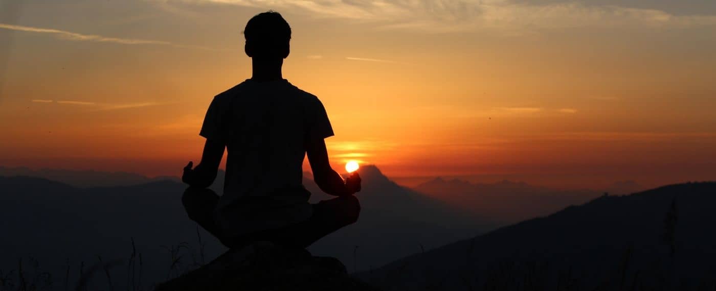 Man sitting on mountain top meditating as the sun sets