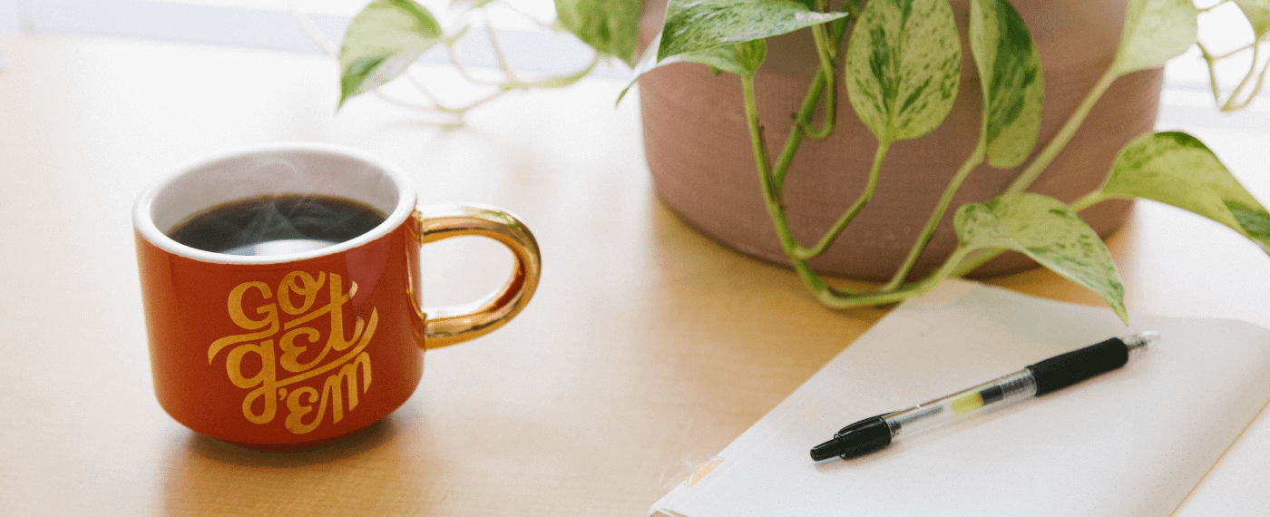 S teaming cup of coffee next to a notepad and pen
