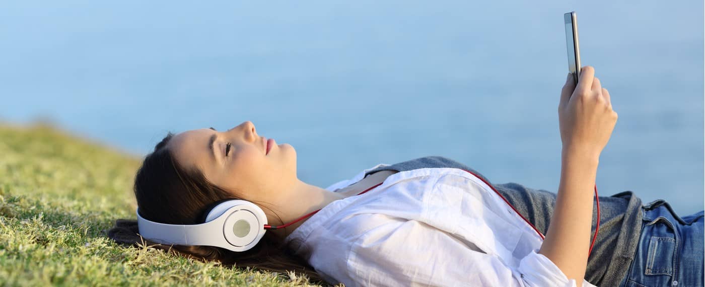 Girl lying on a grassy field with headphones listening to meditation playlist