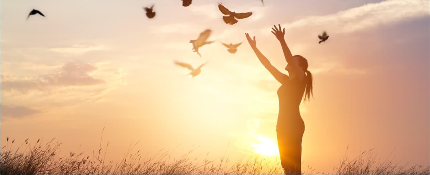 Woman letting go of a flock of birds during sunset