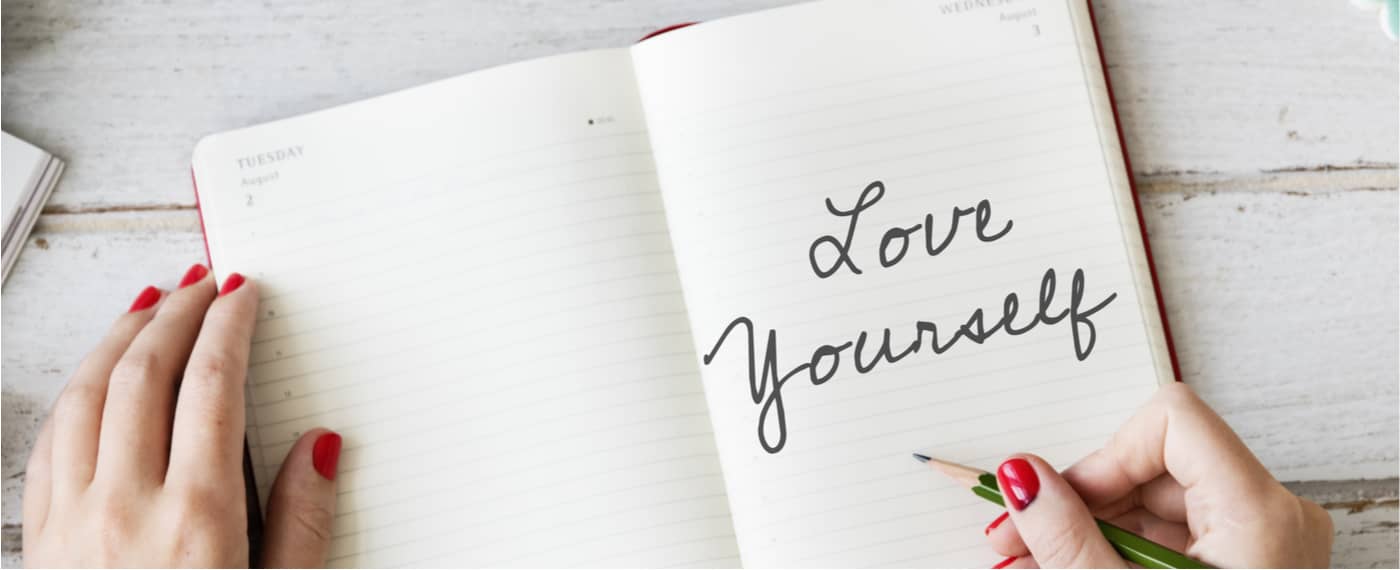 A woman writes "love yourself" in her self-care journal