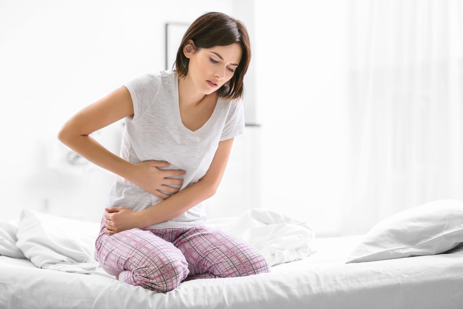 woman kneeling on bed holding her stomach in pain