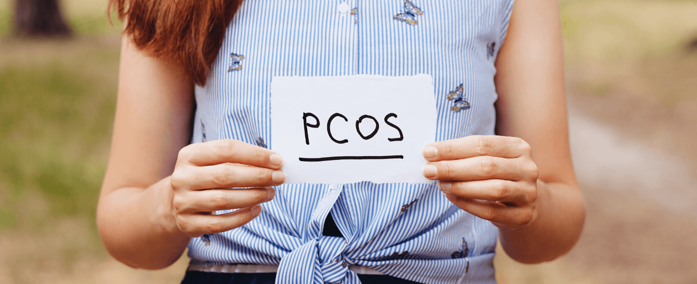 Woman holding a small index card with the letters "PCOS" to promote awareness for polycystic ovarian syndrome