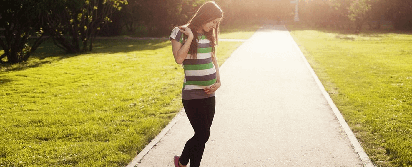 Pregnant woman standing on sunny sidewalk