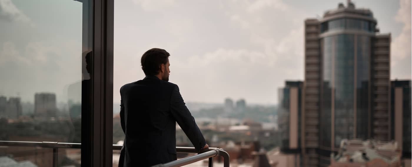 Man in a suit standing on balcony overlooking a city