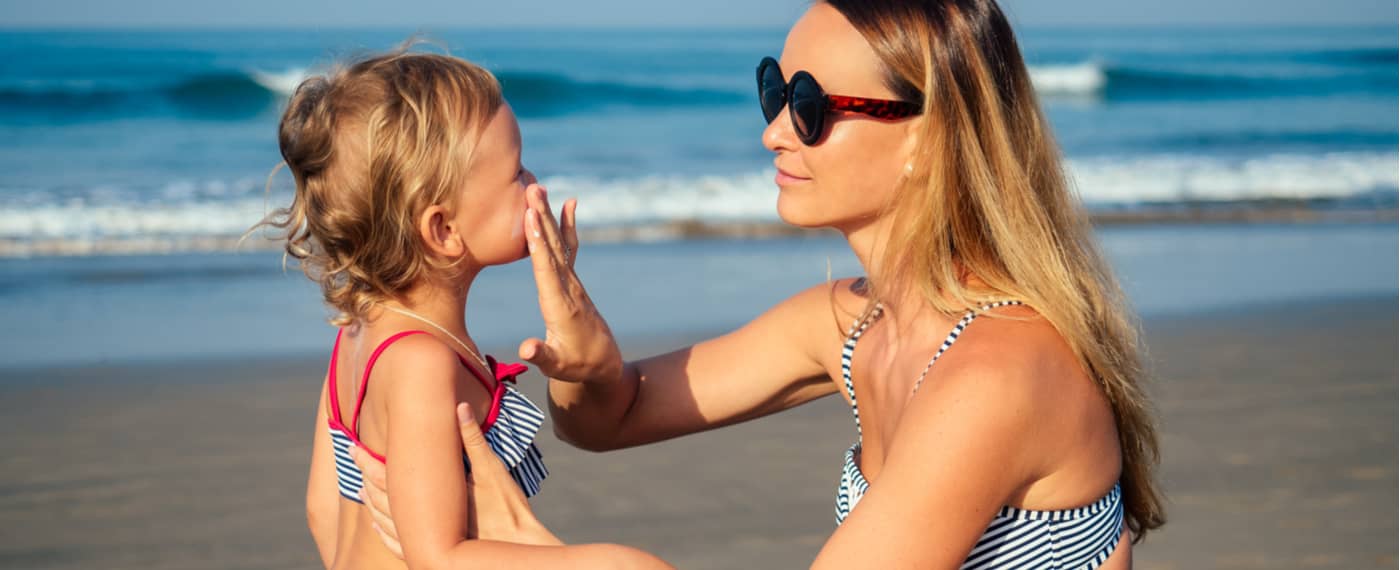 Mother applying sunscreen to small child at the beach