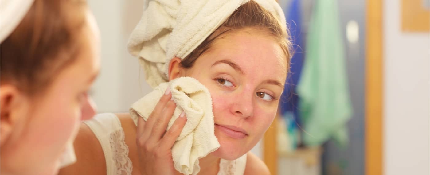 Woman wiping her face with washcloth in the mirror