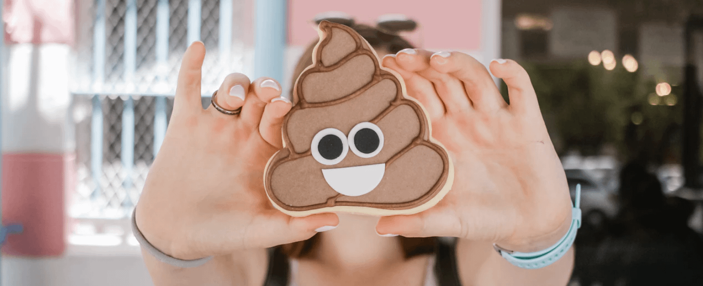 Girl holding up a cookie in the shape of the "poop emoji"