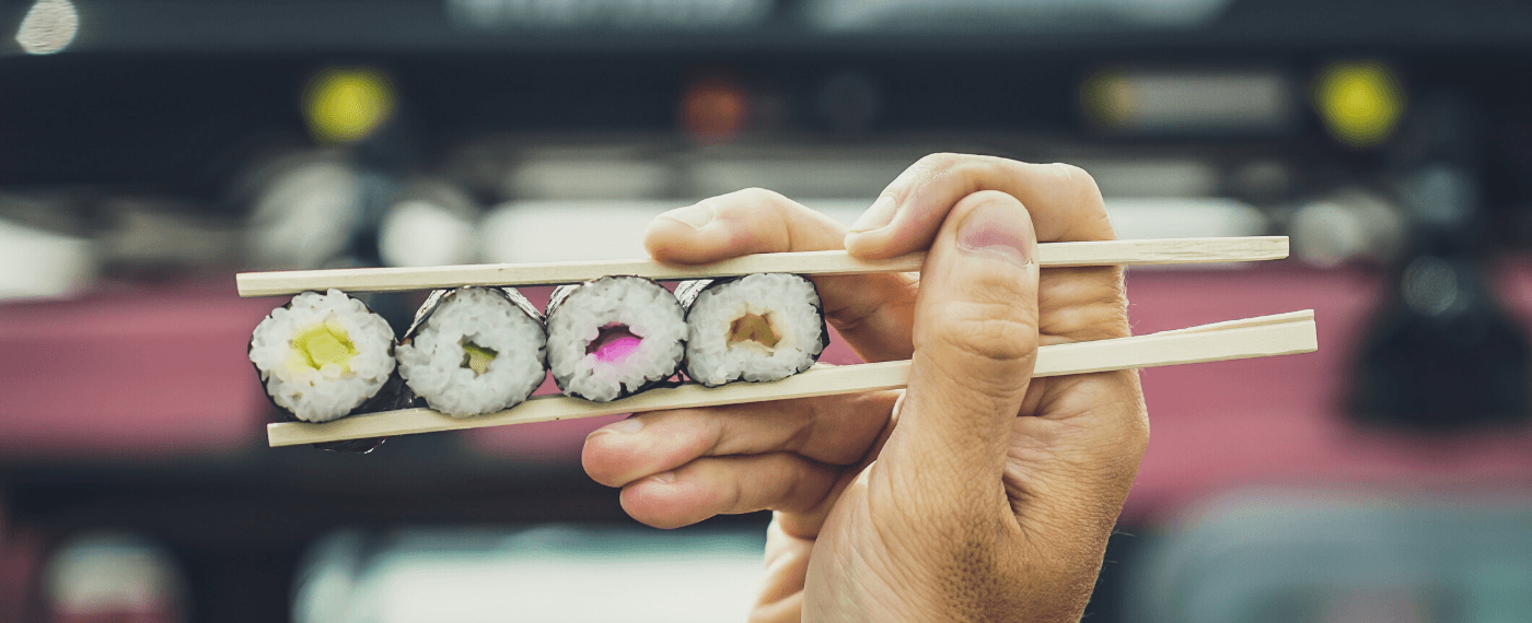 Four sushi rolls in a row being held by one pair of chopsticks