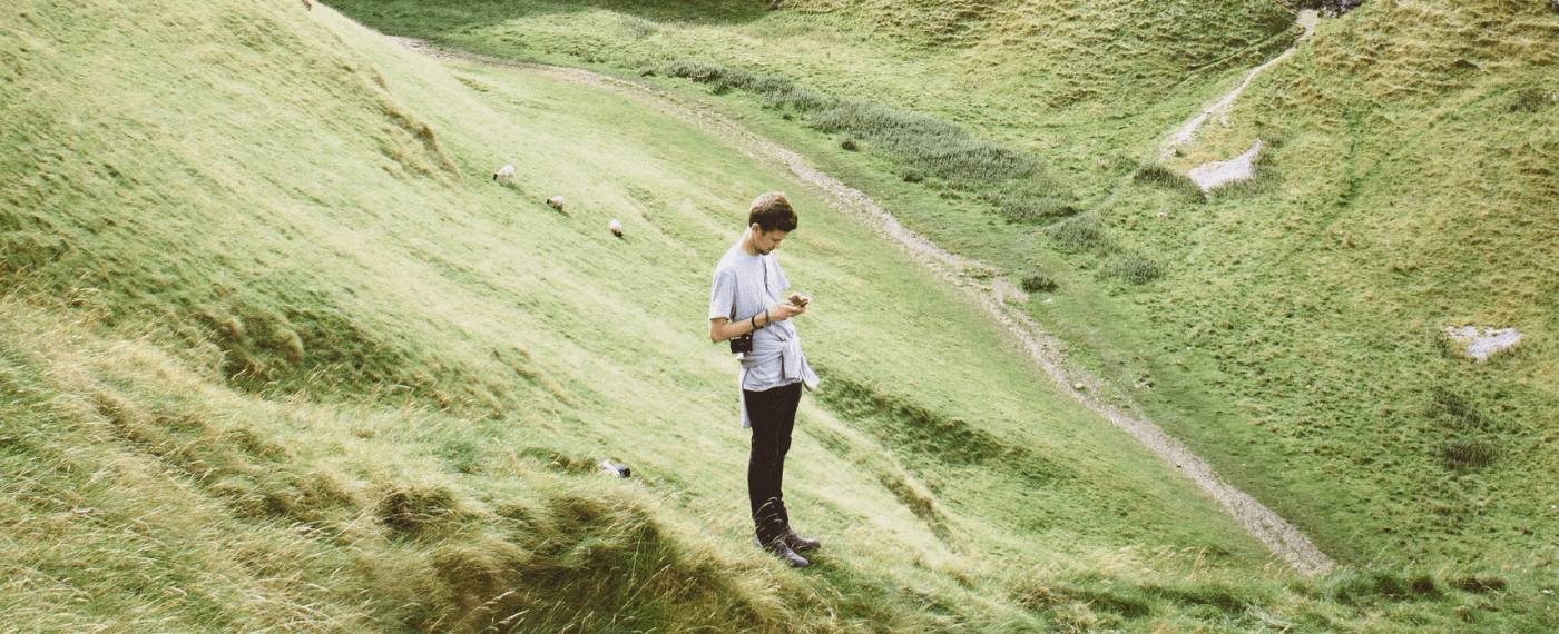 man in the middle of a green field scrolling through his cell phone