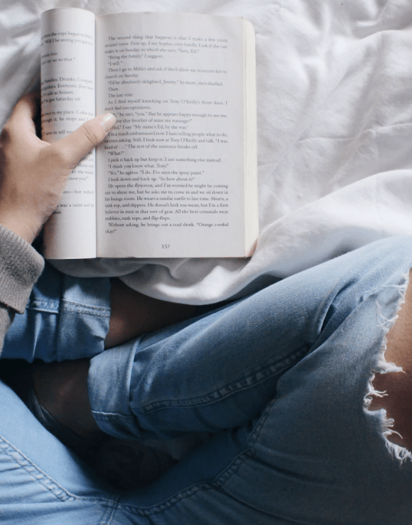 Woman sitting Indian style on bed reading a self-care book