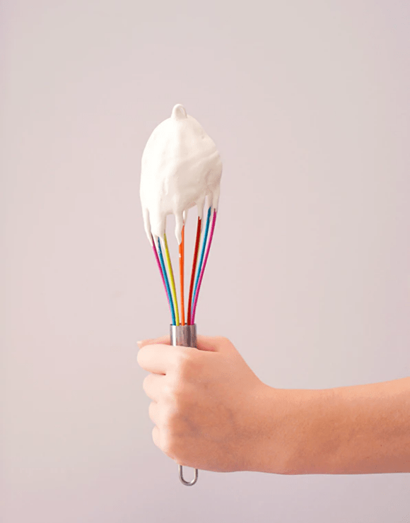 Hand holding a whisk dripping with whipped cream