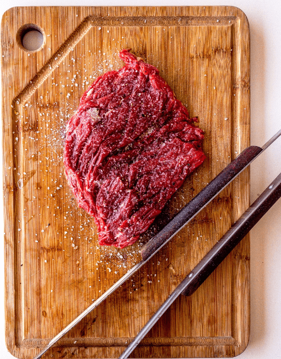 A pound og raw red meat on top of a wooden cutting board