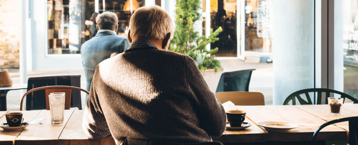 Aging man sitting at a cafe facing out the window