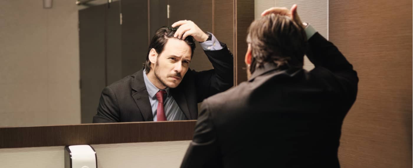 Man in business suit checks his hair line in the bathroom mirror