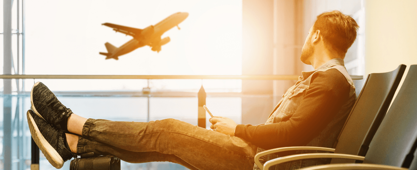 man waiting in airport terminal staring out the window at plane taking off
