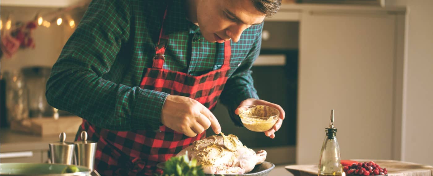 Man with apron on applying applying marinade to chicken