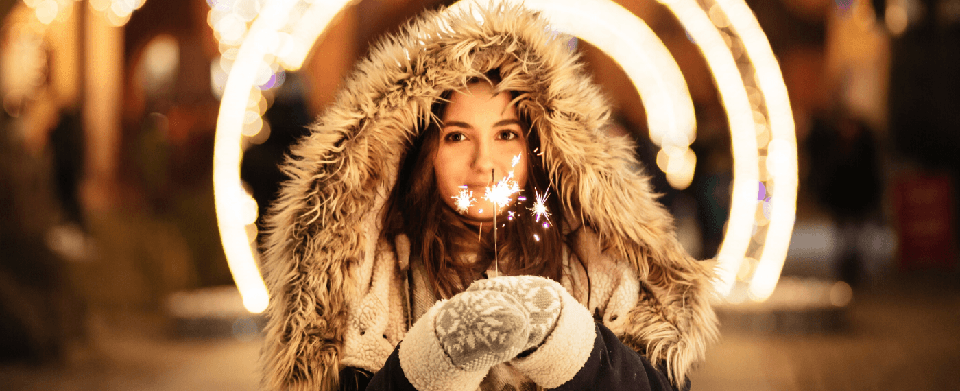 A young girl in a large winter coat holding a lit sparkler