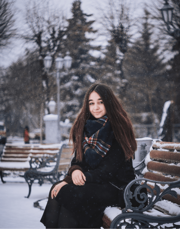young girl smiling and sitting on snowy park bench