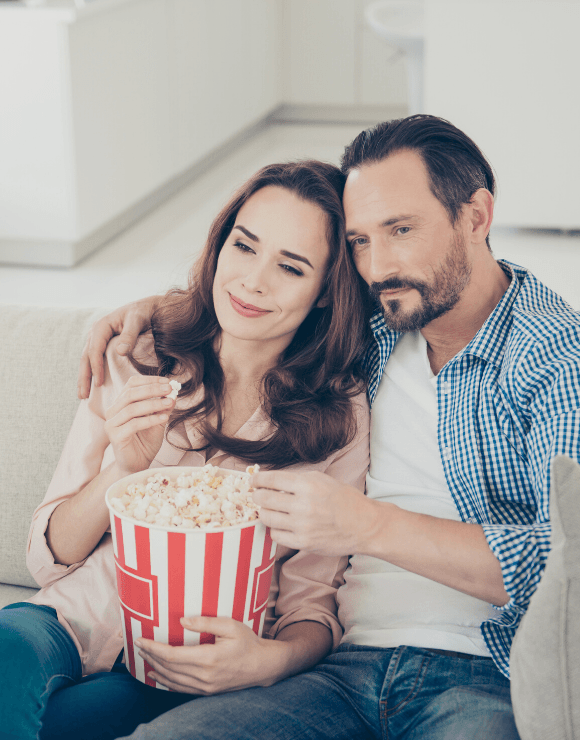 man and woman on couch enjoying a bucket of popcorn
