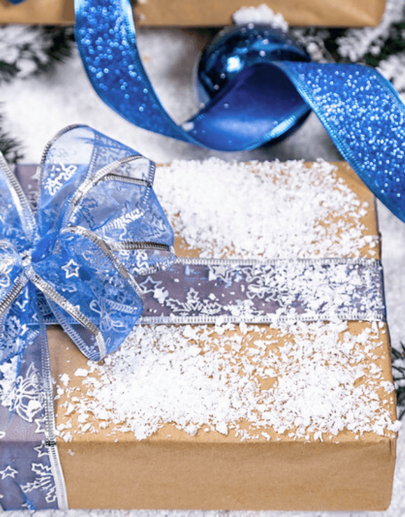 A holiday present wrapped in paper with a ribbon, bow, and snow on top