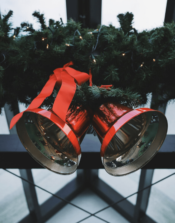 two large holidays bells tied together on a fence by a wreath