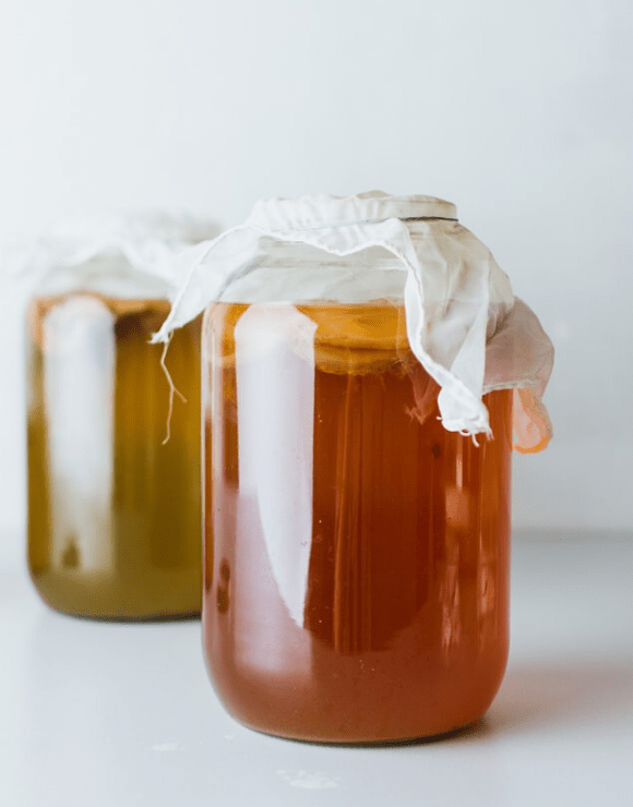 Jars of fermented fruits and herbs known as Kombucha sealed with a cloth lid