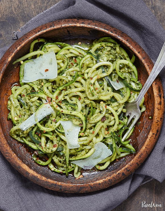 A wooden bowl with pesto zucchini noodles with large slices of parmesan cheese
