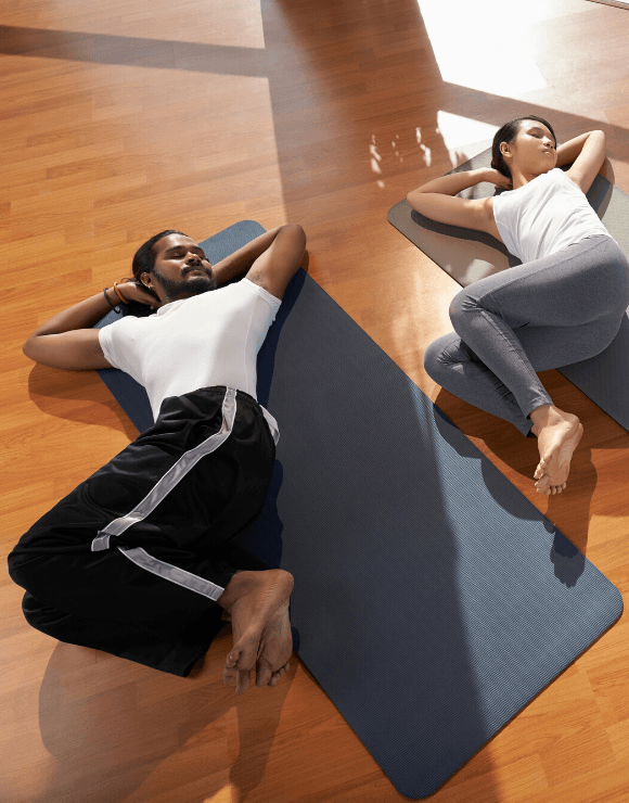 Woman and man lying flat on their backs on a yoga mat stretching their torso to the side