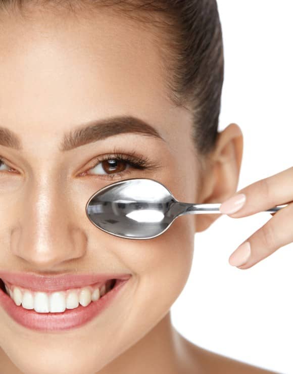 woman applying a cold spoon to her face to help reduce baggy eyes