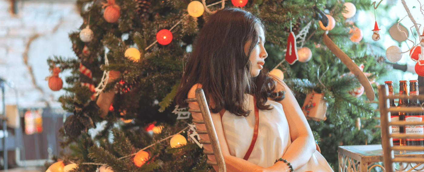 Young girl sitting in front of Christmas tree looking sad being away from home for the holidays